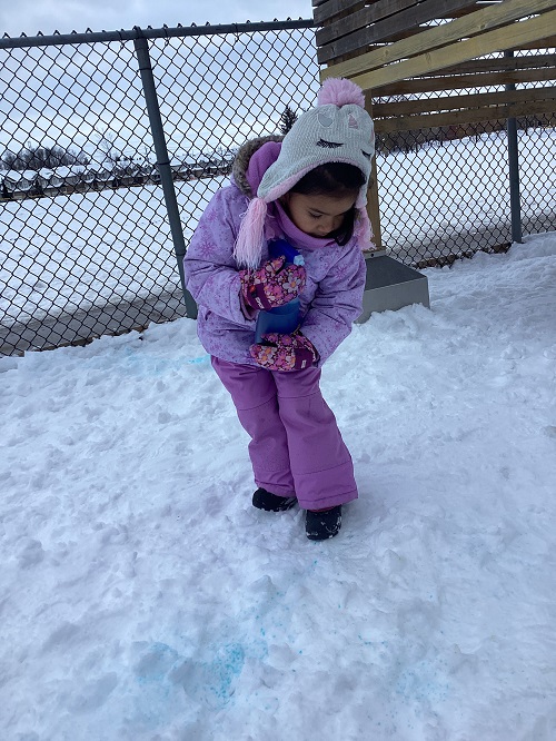 child holding a spray bottle filled with water and food colouring and spraying it on the snow