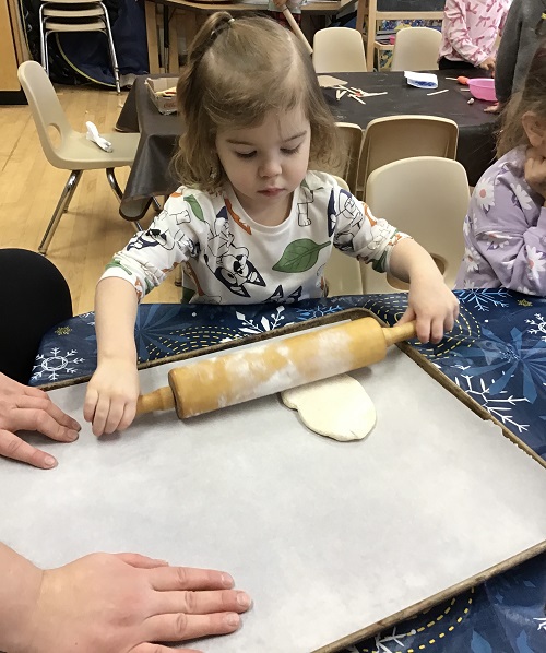 child rolling out pizza dough