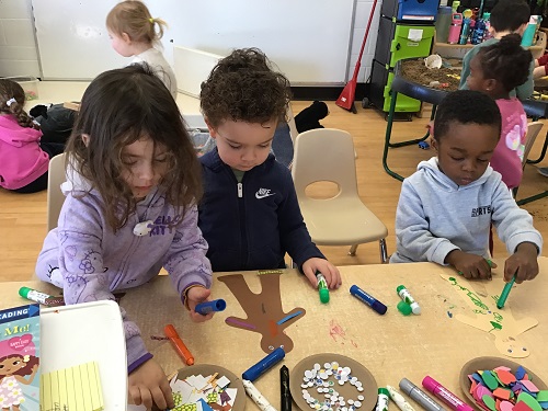 children around a table with art supple creating paper people cut outs