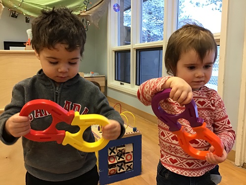 A toddler girl and a toddler boy are using the horseshoe magnets.
