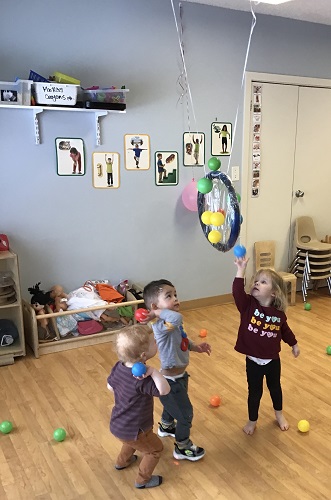 tree toddler with ball all ready to throw them at the hoop. 