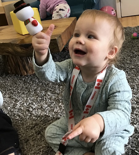 An infant is holding up a snowman finger puppet that they have put on their finger.