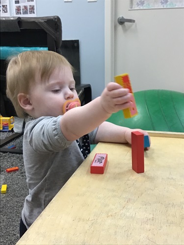 An infant is stacking one coloured block on top of another colored block.