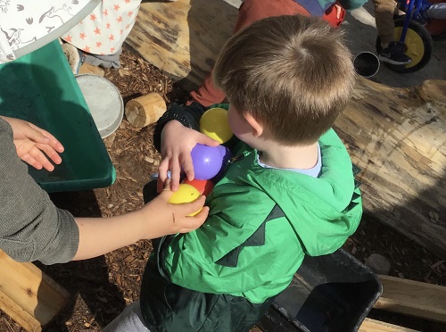 A preschooler is carrying an arm full of colourful balls.