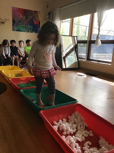 A preschooler is walking through the bins with various loose parts inside them as a group waits for their turn.