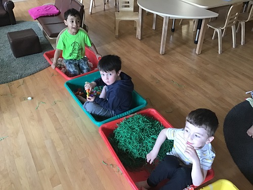 Preschoolers are sitting in bins with various loose parts inside them.