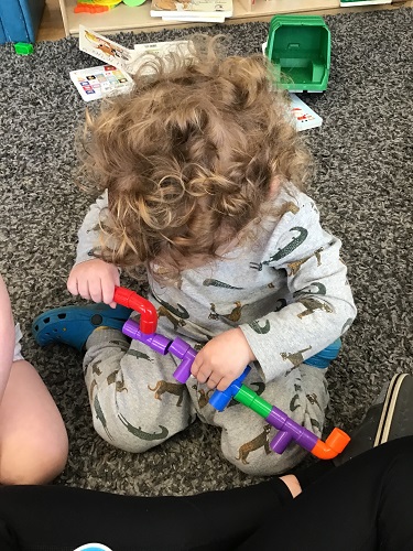 A toddler is conecting some tube blocks together.