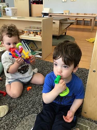 Two toddlers are blowing into their tube block creations as if they were horns.