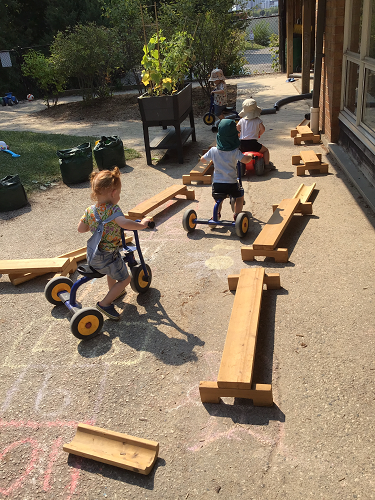 Three toddlers are riding bikes through their toddler track.