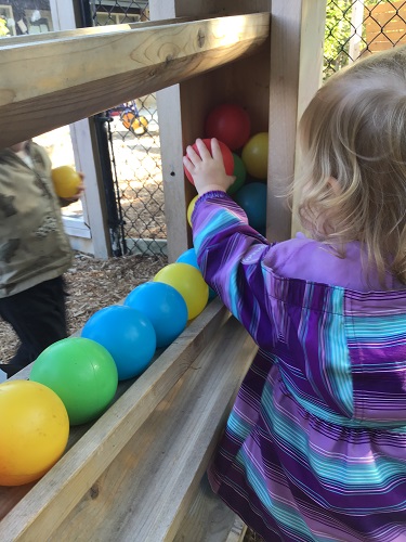 A toddler is adding different coloured balls to the ball drop.