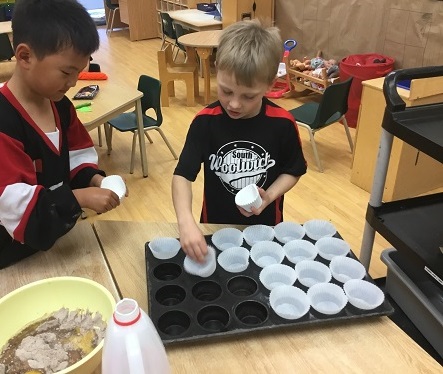 2 school-age boy lining cupcake tray