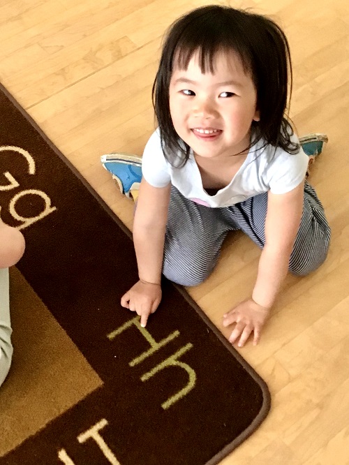 child pointing to the letter H on the carpet