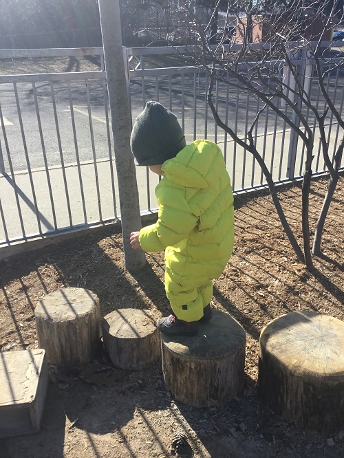 child walking across wooden log outside on the playground