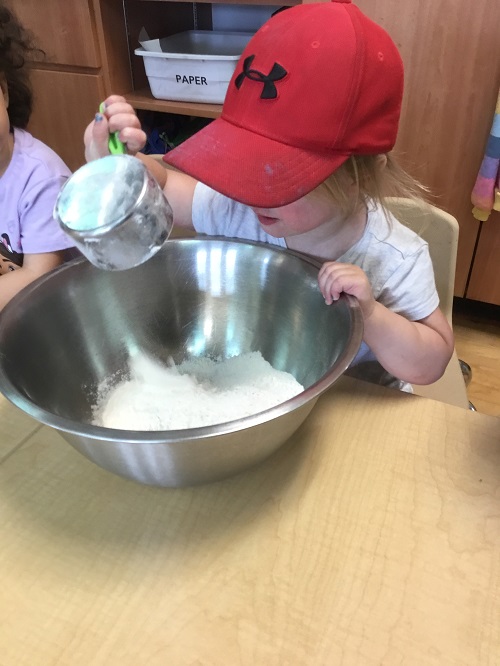 child putting in flour into a mixing bowl