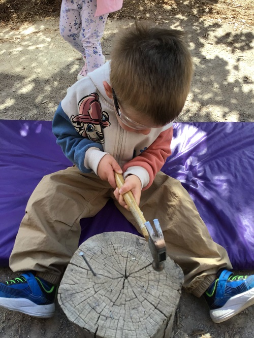 child using a hammer onto a piece of wood