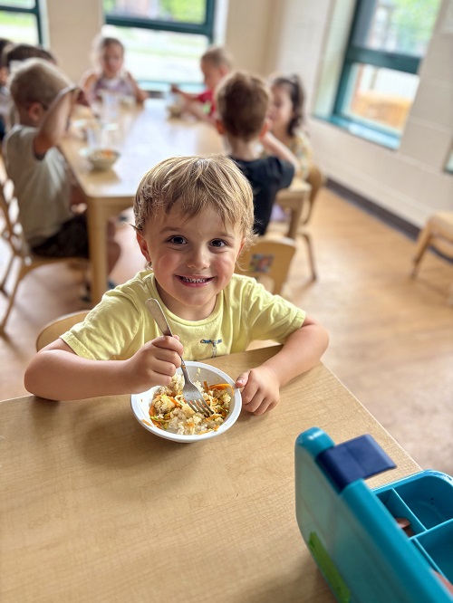 A child smiling as they eat their delicious meal