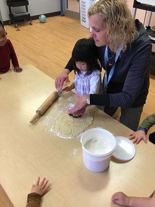 Child cutting a shape out of dough with educator.