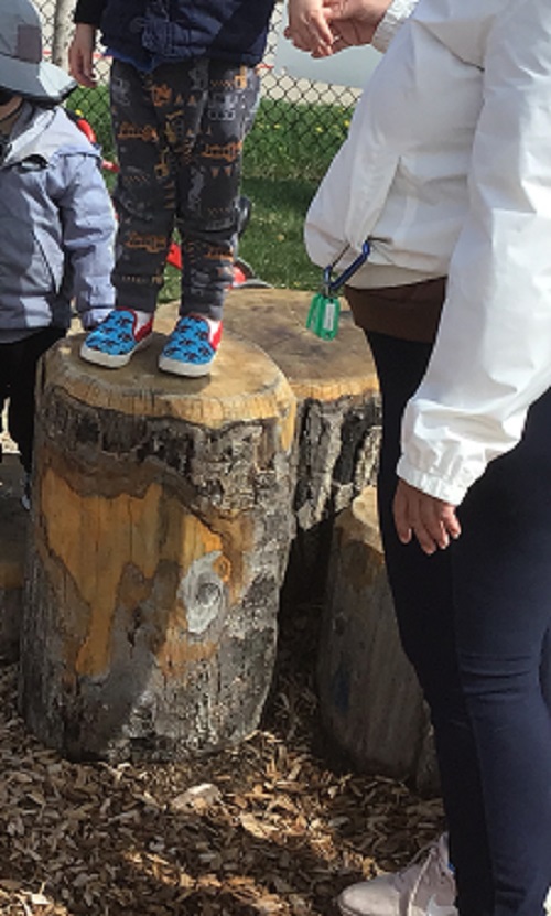Child about to jump off a log with educator help.