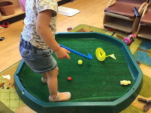 Child pretending to play golf on the tuff tray. 