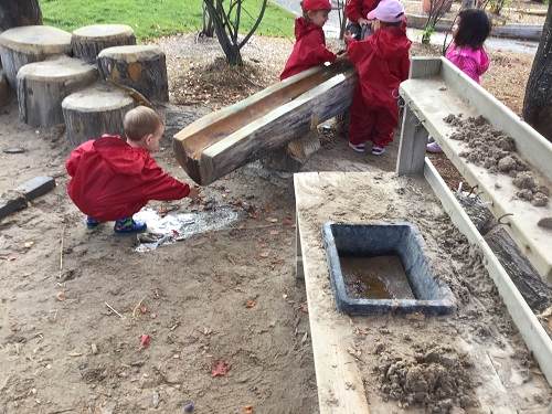 Children creating mud with sand and water from water feature. 