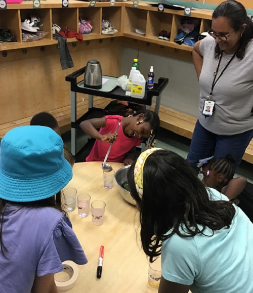 Child pouring the cabbage water into a cup while peers observe.