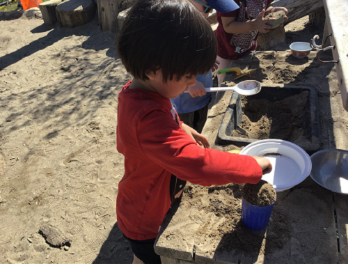 Child pretending to cook in the sandbox.