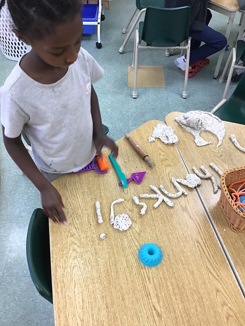 Child creating letters with playdough.