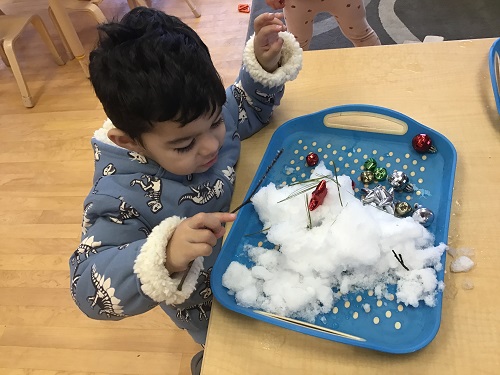 Child placing a small branch into snow on a tray, indoors.