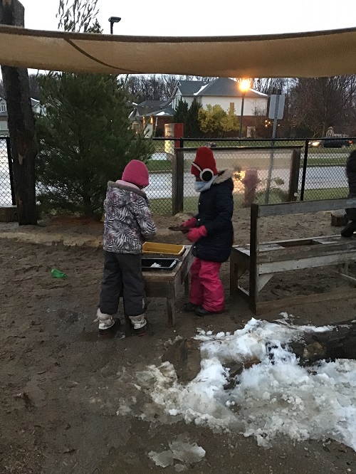 Children mixing snow on the playground mud kitchen