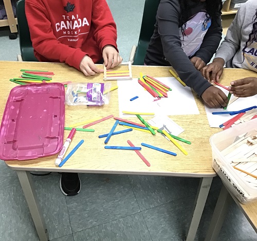 Children creating on table with coloured popsicle sticks.