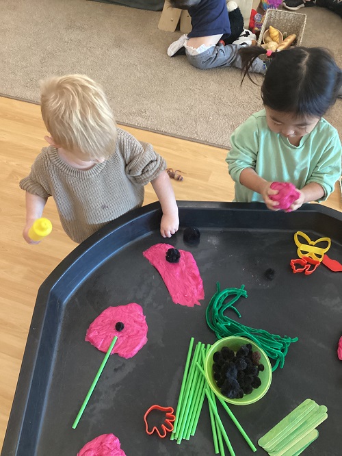 2 toddler children playing with playdough on the tuff tray