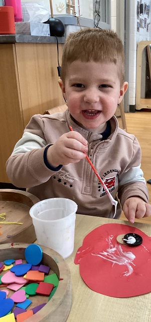 A preschool child gluing foam shapes onto a piece of construction paper