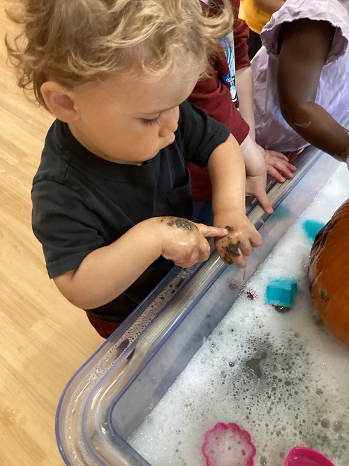 A toddler looking at the mud on their hands