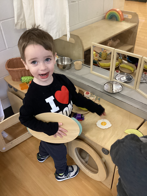 A toddler child in the dramatic play area using pretend food