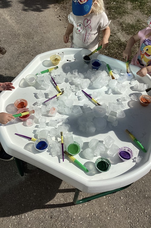 A group of toddlers painting ice on the tuff tray