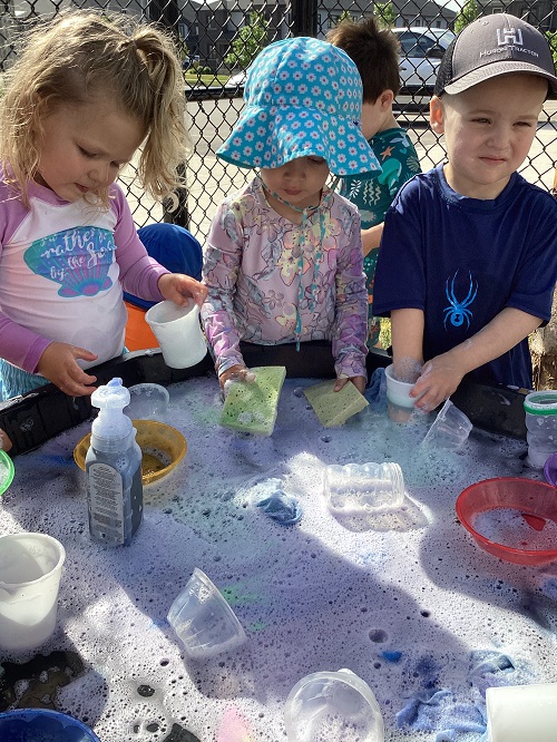 Three children exploring foam with different items.