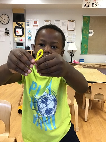 Preschool child bending a yellow pipe cleaner to create a fish shape