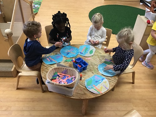 Group of Preschool age children sitting at a round table together creating aquariums with loose creative materials