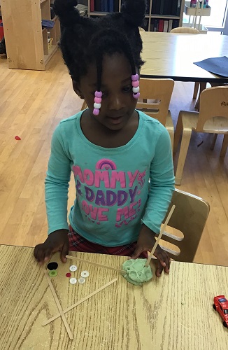 Preschool child using playdough, sticks and buttons to create an insect 