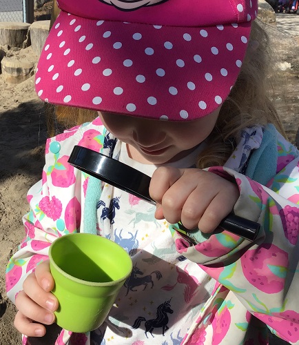 Preschool child using a magnifying glass to take a closer look at and insect in a cup