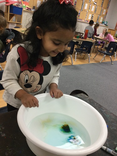 A child looking into a bucket to see the colours spread in the water