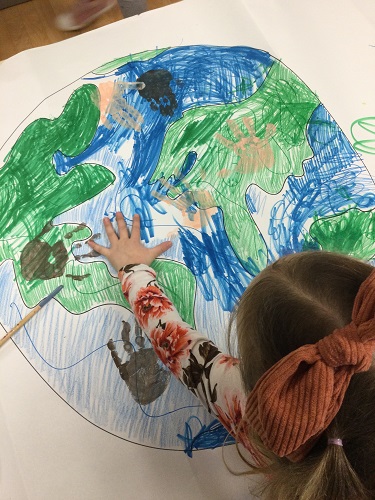 A school aged child adding her hand print to a picture of the world