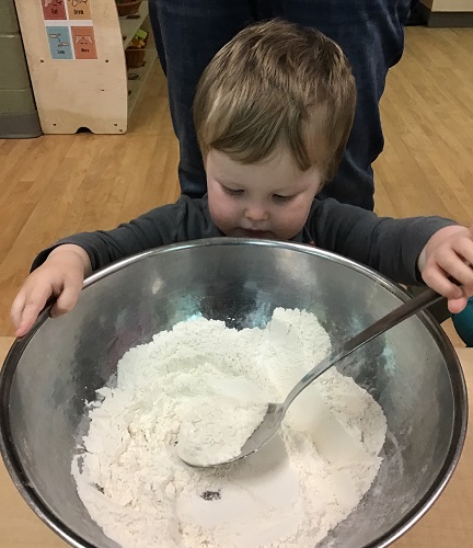 A child stirring a large bowl of flour fot the class to make playdough together