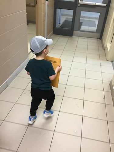 Child walking down the hall holding an envelope 