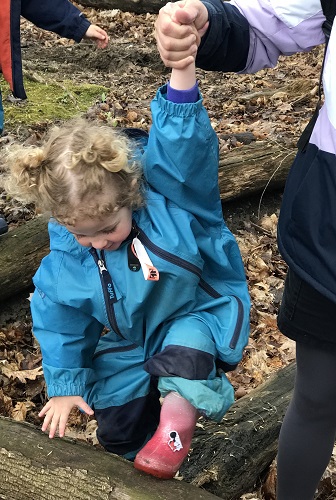 An educator helping a child up onto a log
