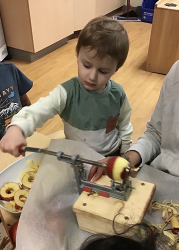 A child using an apple peeler with the help of an educator