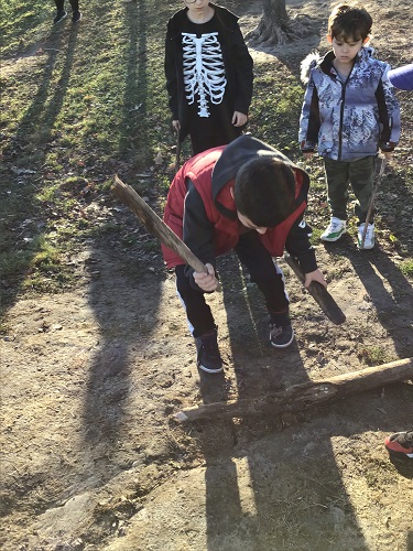A child using a small stick to hit a large log