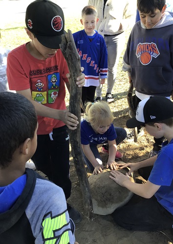 School age children working together to move a big rock from the ground