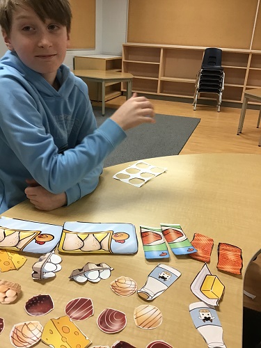 A school aged child sitting at a talbe with paper food