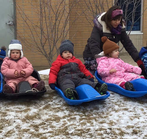 Three children sitting in sleds waiting to slide down the hill
